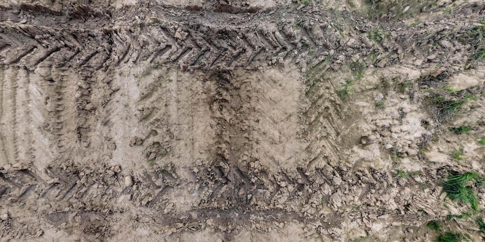 visie van bovenstaand Aan structuur van nat modderig weg met trekker band sporen in platteland foto