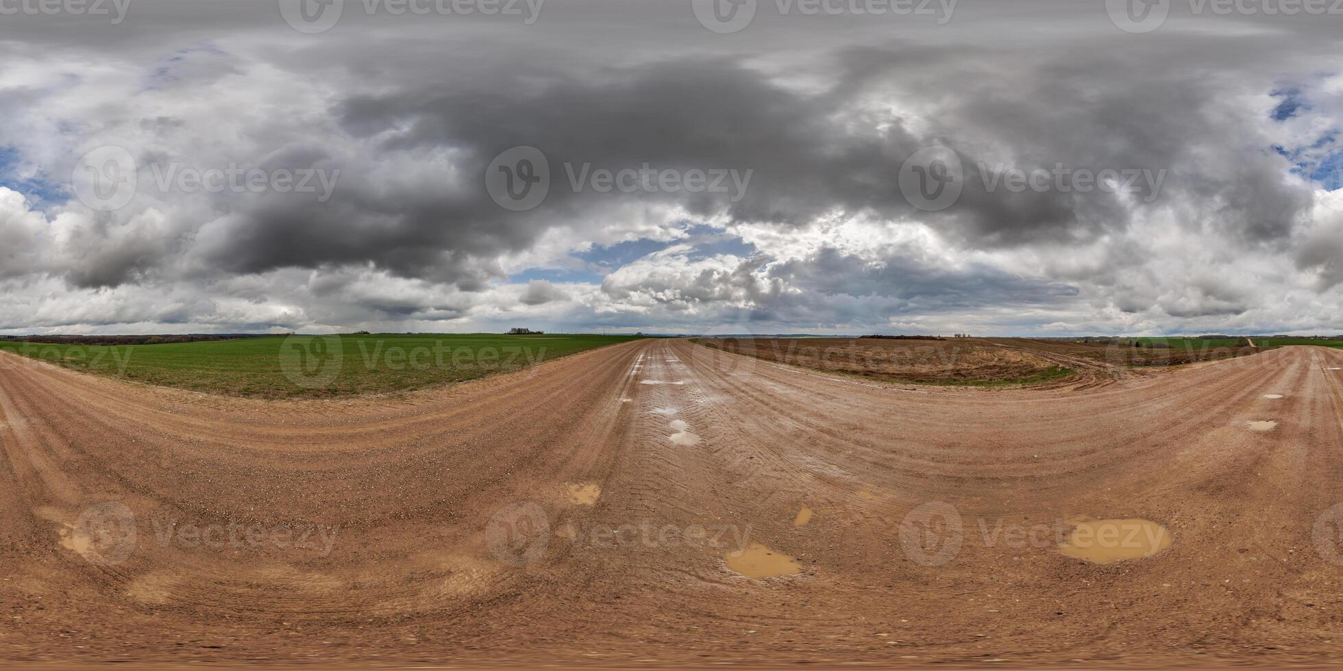 hdri 360 panorama Aan nat grind weg met plassen tussen velden in voorjaar naar dag met storm wolken in equirectangular vol naadloos bolvormig projectie, voor vr ar virtueel realiteit inhoud foto