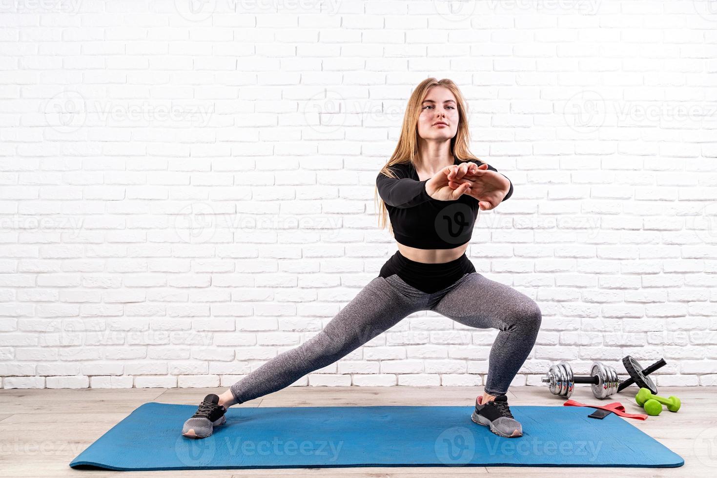 jonge fitte vrouw doet zijwaartse lunges binnenshuis op een fitnessmat foto