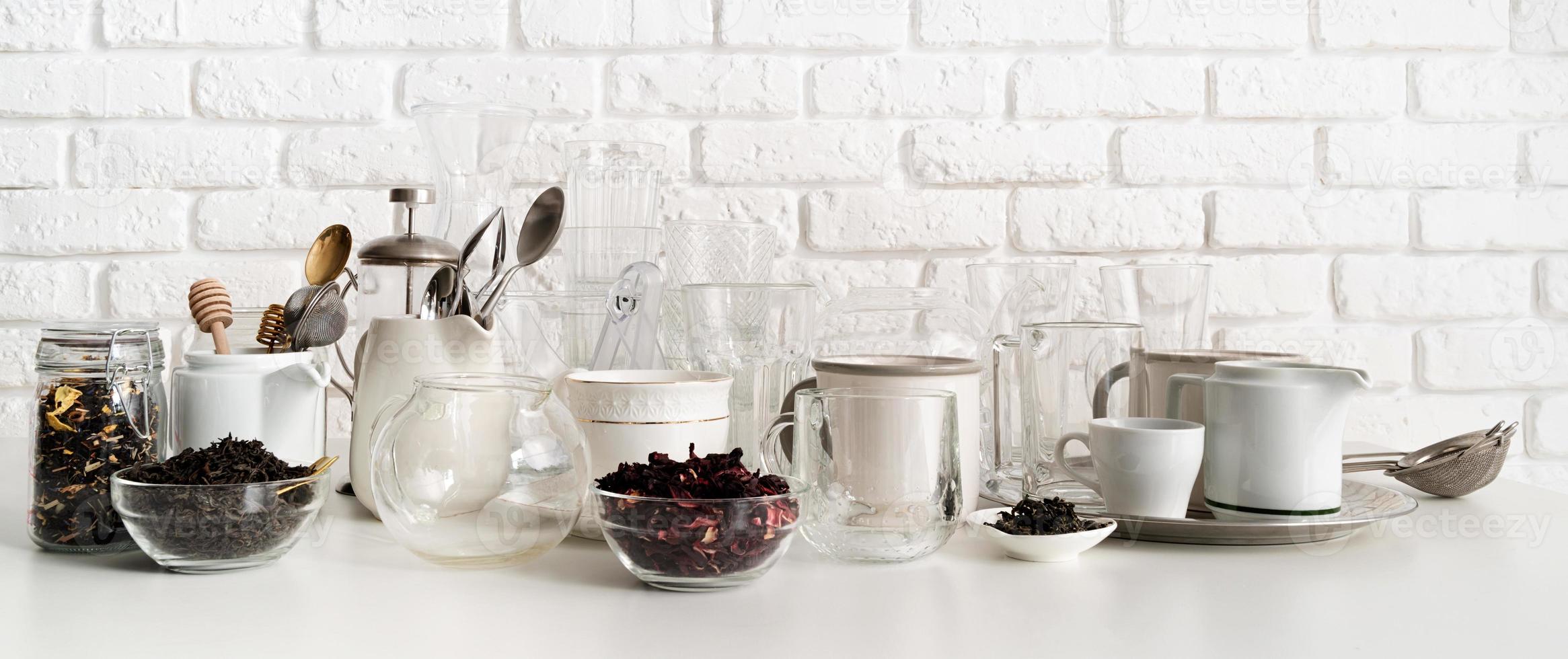 keramische en glazen kopjes en servies op tafel op witte bakstenen muur achtergrond foto