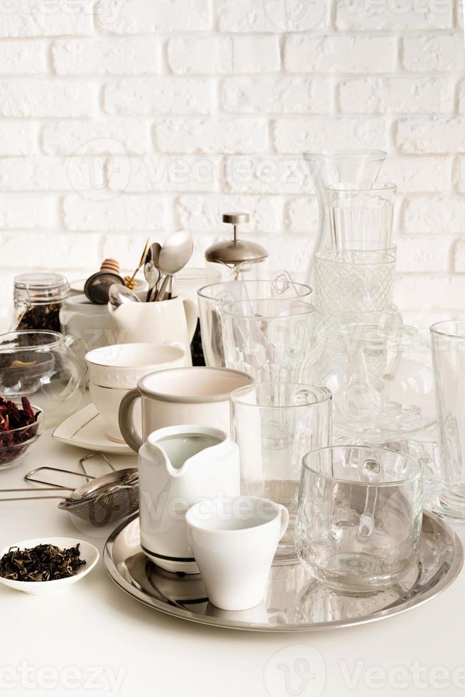 keramische en glazen kopjes en servies op tafel op witte bakstenen muur achtergrond foto