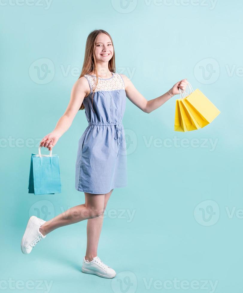 gelukkige jonge vrouw met boodschappentassen geïsoleerd op blauwe achtergrond foto