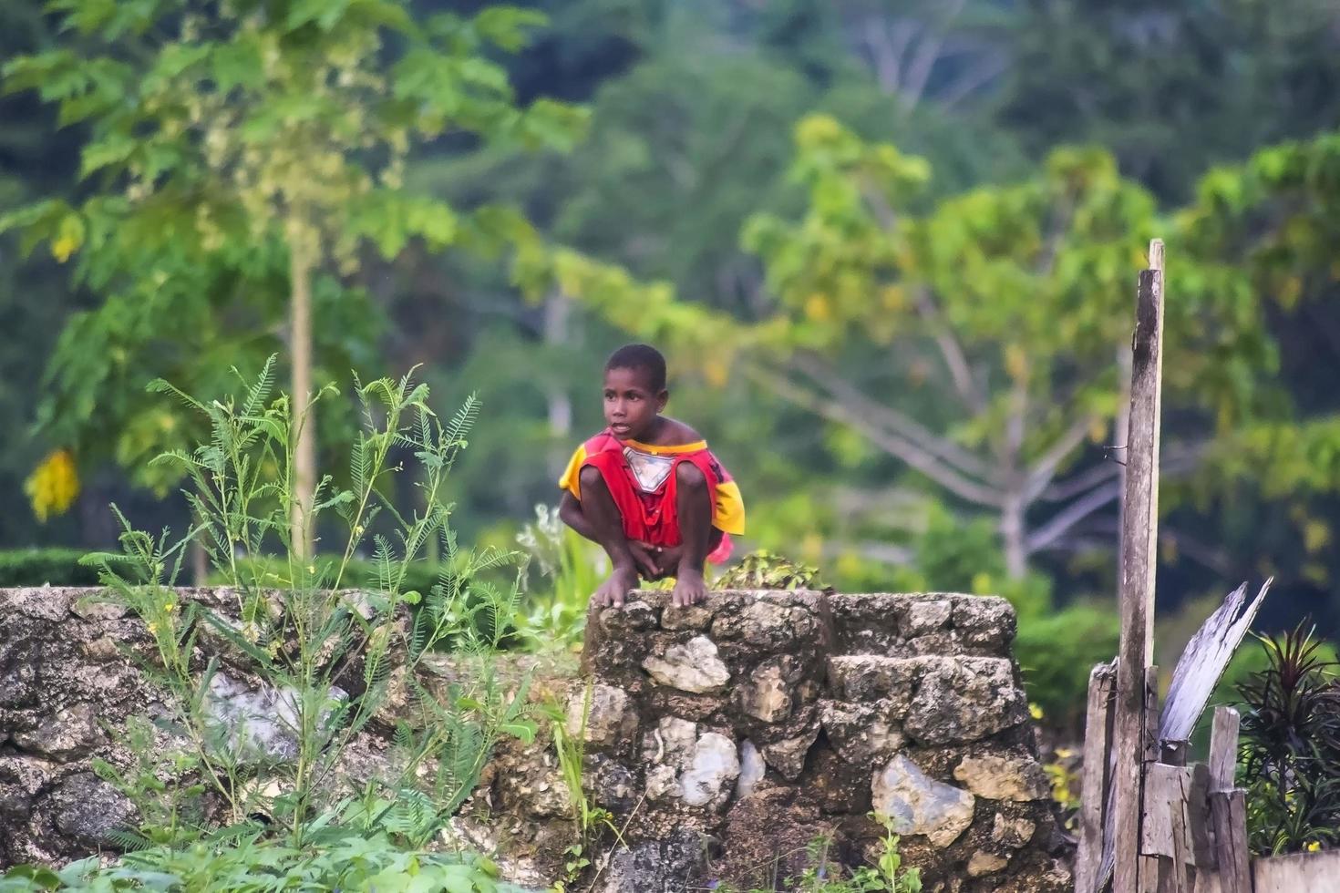 sorong, West Papoea, Indonesië, 2021. een kleine jongen hurkt op een stenen fundering in een eenzame vallei foto