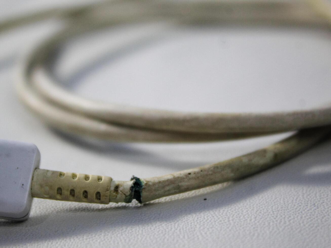 dichtbij omhoog de wit gebroken smartphone USB kabel Aan wit houten achtergrond. foto