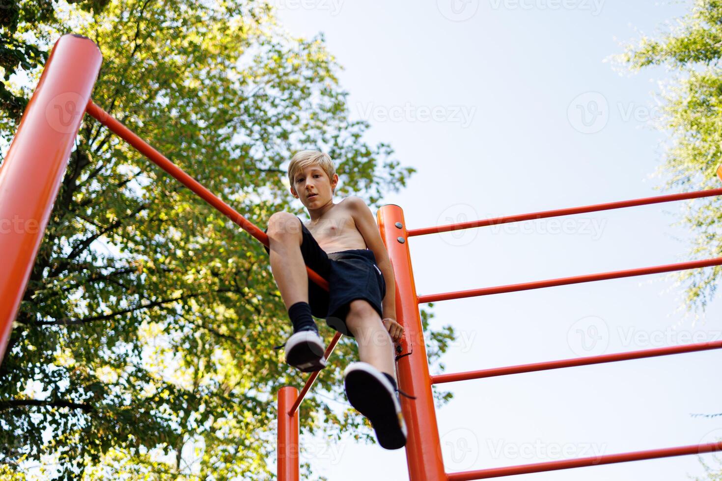 visie van hieronder van een tiener zittend Aan een gymnastiek bar en aan het kijken de actie. straat training Aan een horizontaal bar in de school- park. foto