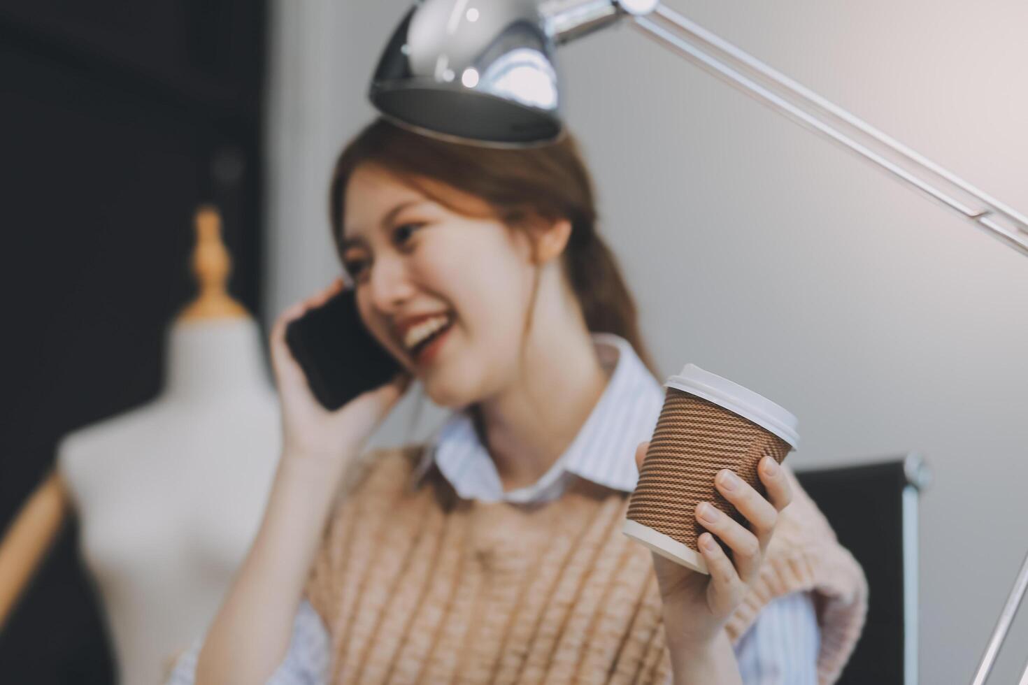 Aziatisch volwassen vrouw mode ontwerper werken in creatief studio, drinken koffie, overweegt en denken van ideeën, in beeld brengen jurk ontwerp verzameling, en professioneel winkel kleermaker mkb ondernemer. foto