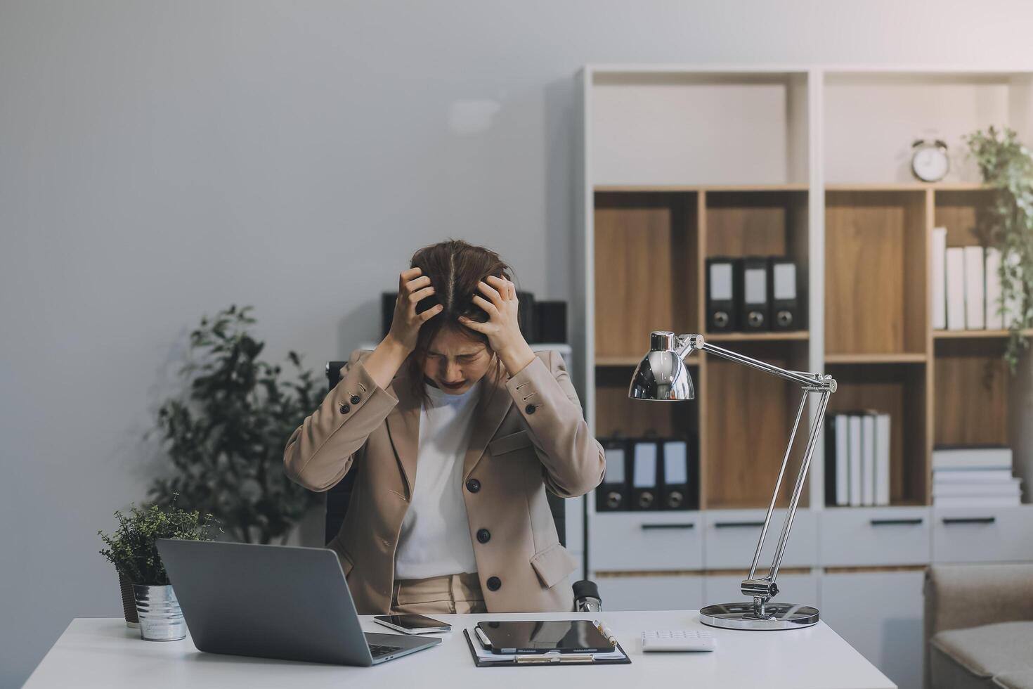 Aziatisch Dames zittend in een kantoor met spanning en oog spanning moe, portret van verdrietig ongelukkig moe gefrustreerd teleurgesteld dame lijden van migraine zittend Bij de tafel, ziek arbeider concept foto