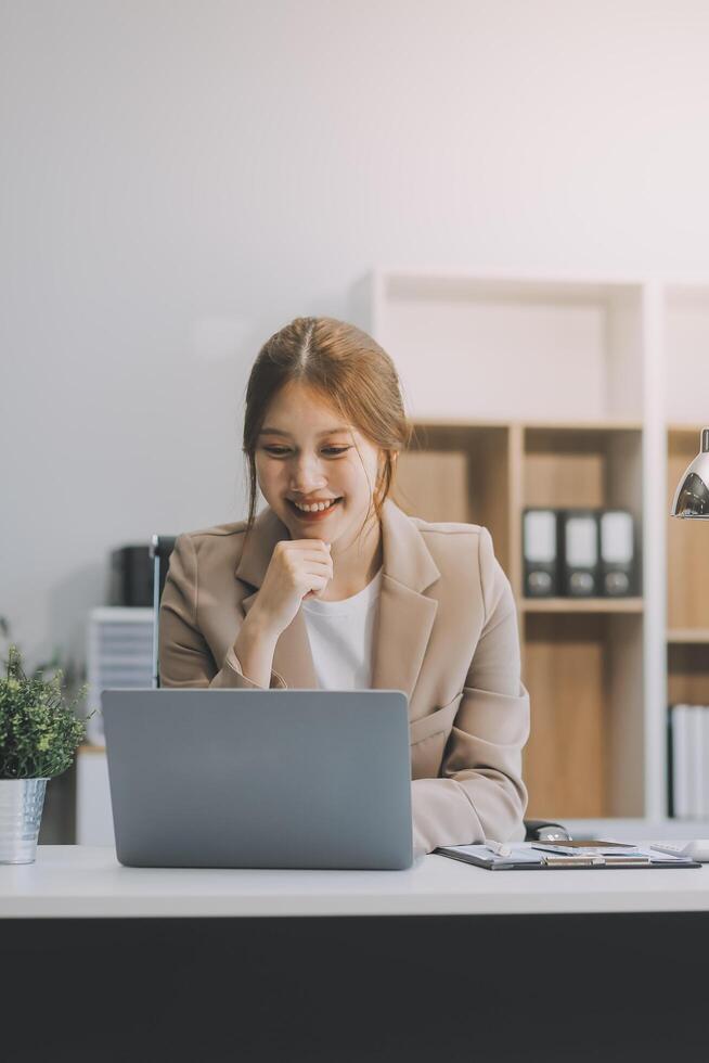 Aziatische zakenvrouw die een laptopcomputer gebruikt en op kantoor werkt met een rekenmachinedocument op het bureau, planning analyseert van het financiële rapport, businessplaninvestering, financiële analyseconcept. foto