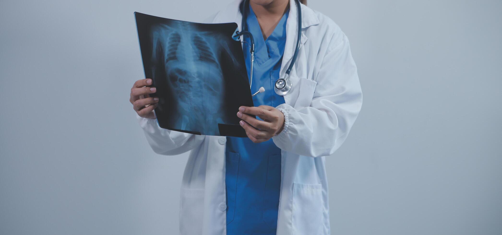 Aziatisch moslim dokter in hijab en scrubs hoofdtelefoons in de omgeving van haar nek staan vol vertrouwen in de medisch kantoor, geïsoleerd Aan wit achtergrond, Holding röntgenstraal film. foto