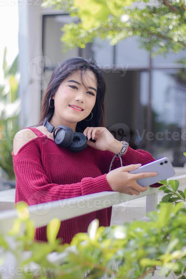 portret van mooi sexy Aziatisch vrouw verkennen cafe buitenshuis. meisje zittend glimlachen draag- een mobiele telefoon apparaatje op zoek Bij de camera foto