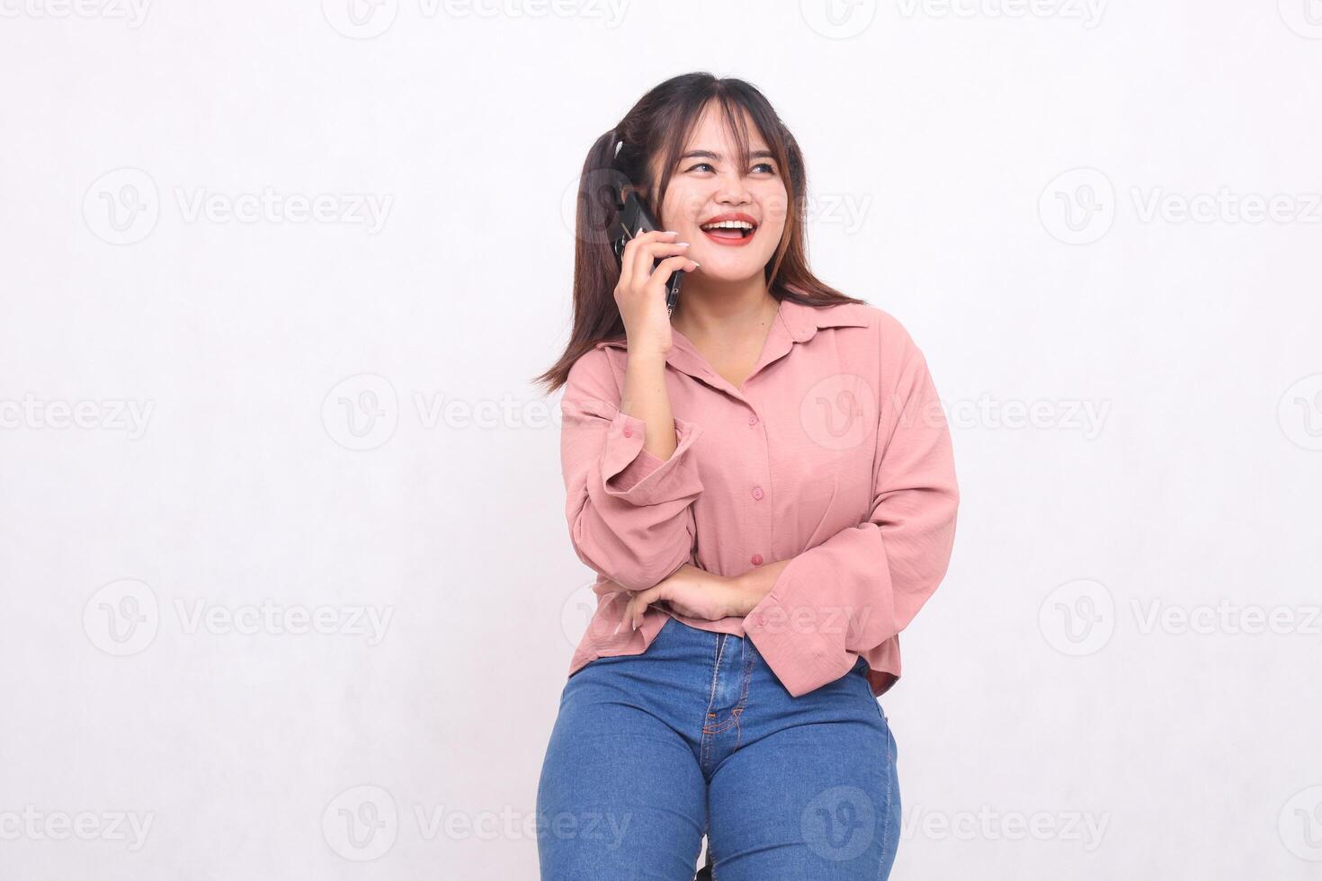 mooi gelukkig Aziatisch vrouw in haar Jaren 20 vervelend gewoontjes overhemd met armen gekruiste gebruik makend van cel telefoon telefoon houding terwijl lachend op zoek links Aan wit achtergrond studio portret voor banier advertentie, banier foto