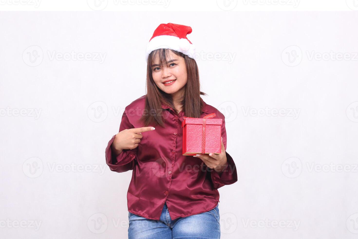 portret van een mooi, vrolijk Aziatisch meisje in haar Jaren 20 draag- Verpakt cadeaus Bij kerstmis, de kerstman claus hoed, modern glimmend rood shirt, tonen cadeaus Aan een wit achtergrond voor Promotie en reclame foto