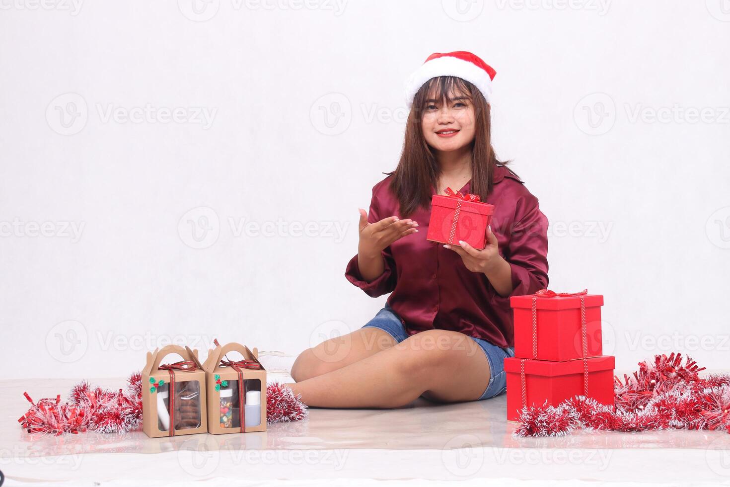 vrolijk jong mooi zuidoosten Aziatisch meisje introduceert doos De volgende naar 3 geschenk dozen van belemmert Bij Kerstmis vervelend de kerstman hoofdband en rood overhemd Aan wit achtergrond voor Promotie en reclame foto
