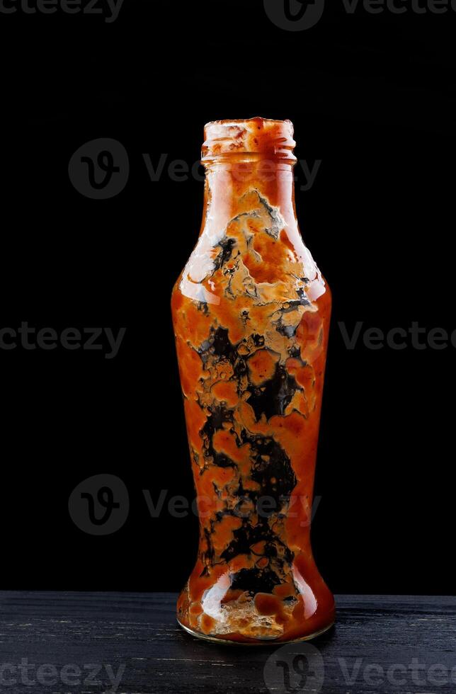 tomaat saus . leeg ketchup fles. glas fles met resterend ketchup binnen Aan een zwart achtergrond. foto