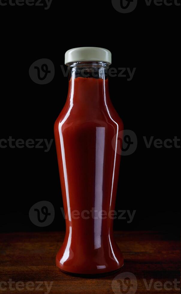 fles van tomaat saus Aan een donker achtergrond. ketchup in een glas fles Aan een houten bord. foto