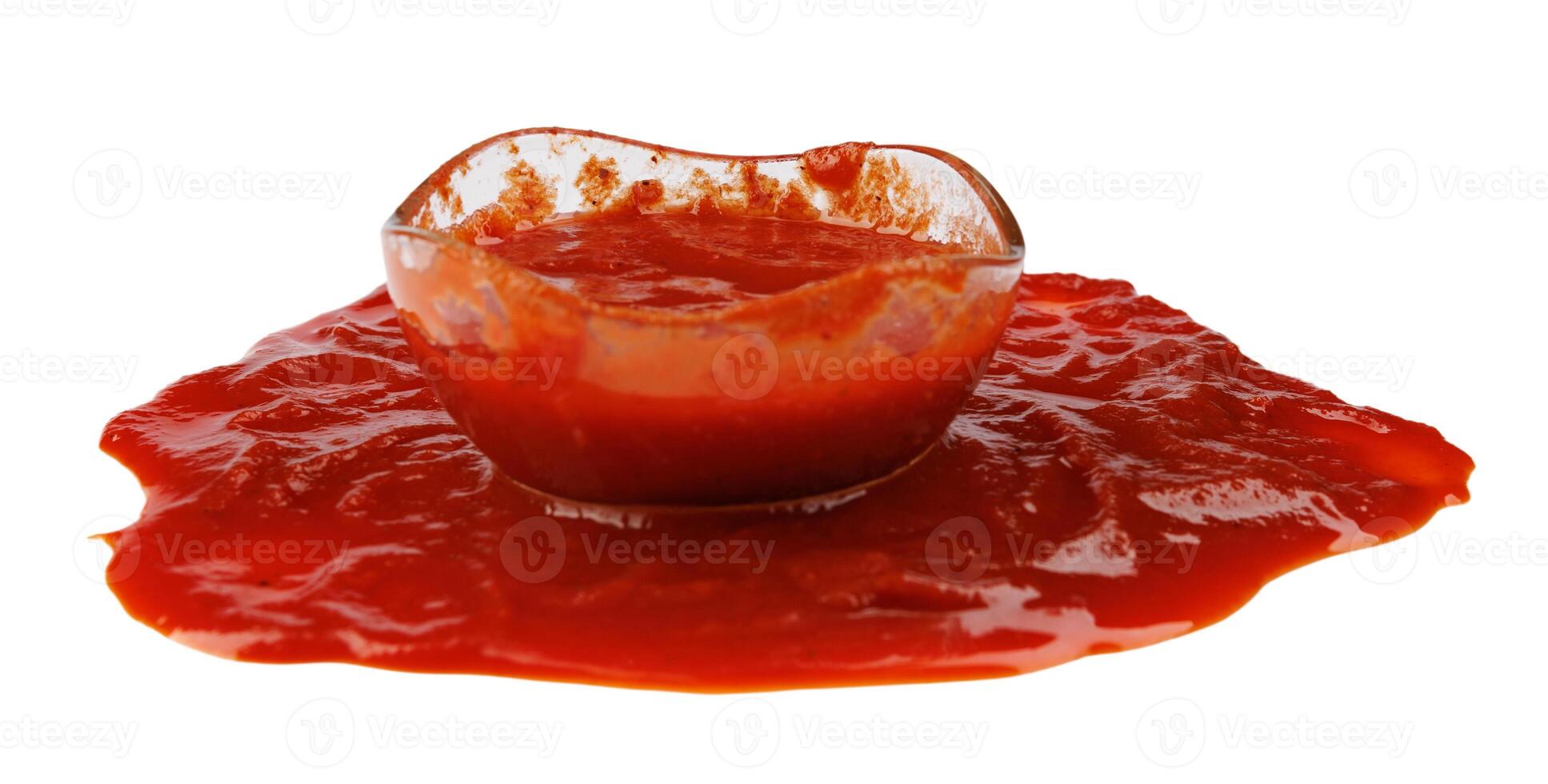 tomaat saus . glas kop met ketchup en een plas van ketchup gemorst in de omgeving van het geïsoleerd Aan een wit achtergrond. foto