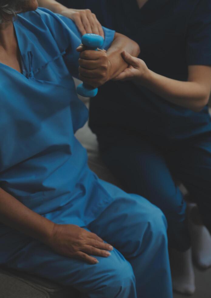 oud vrouw opleiding met fysiotherapeut gebruik makend van halters Bij huis. therapeut assisteren senior vrouw met opdrachten in verpleging huis. ouderen geduldig gebruik makend van halters met uitgestrekt armen. foto