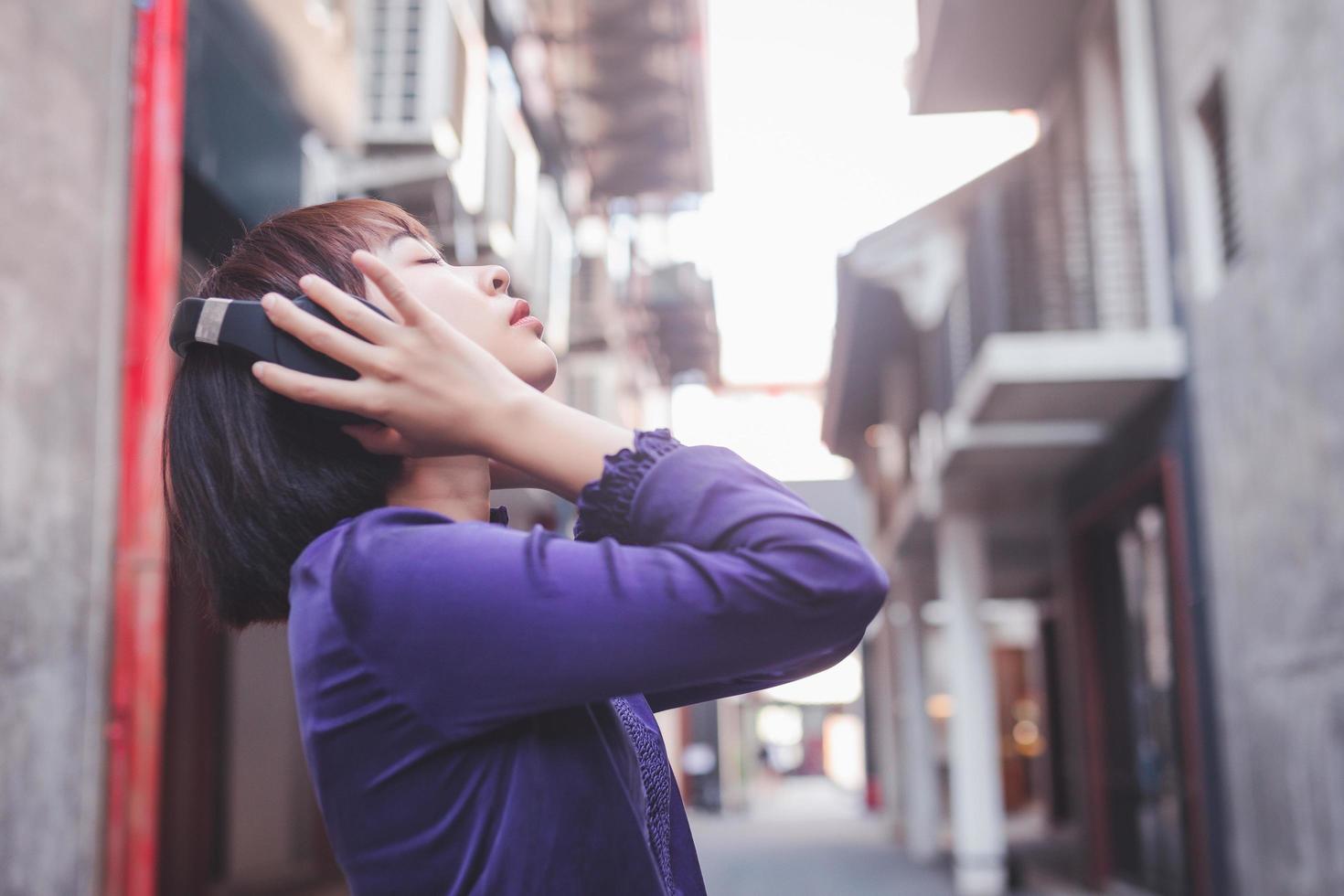 gelukkige jonge aziatische vrouw die op straat naar muziek luistert met een koptelefoon foto