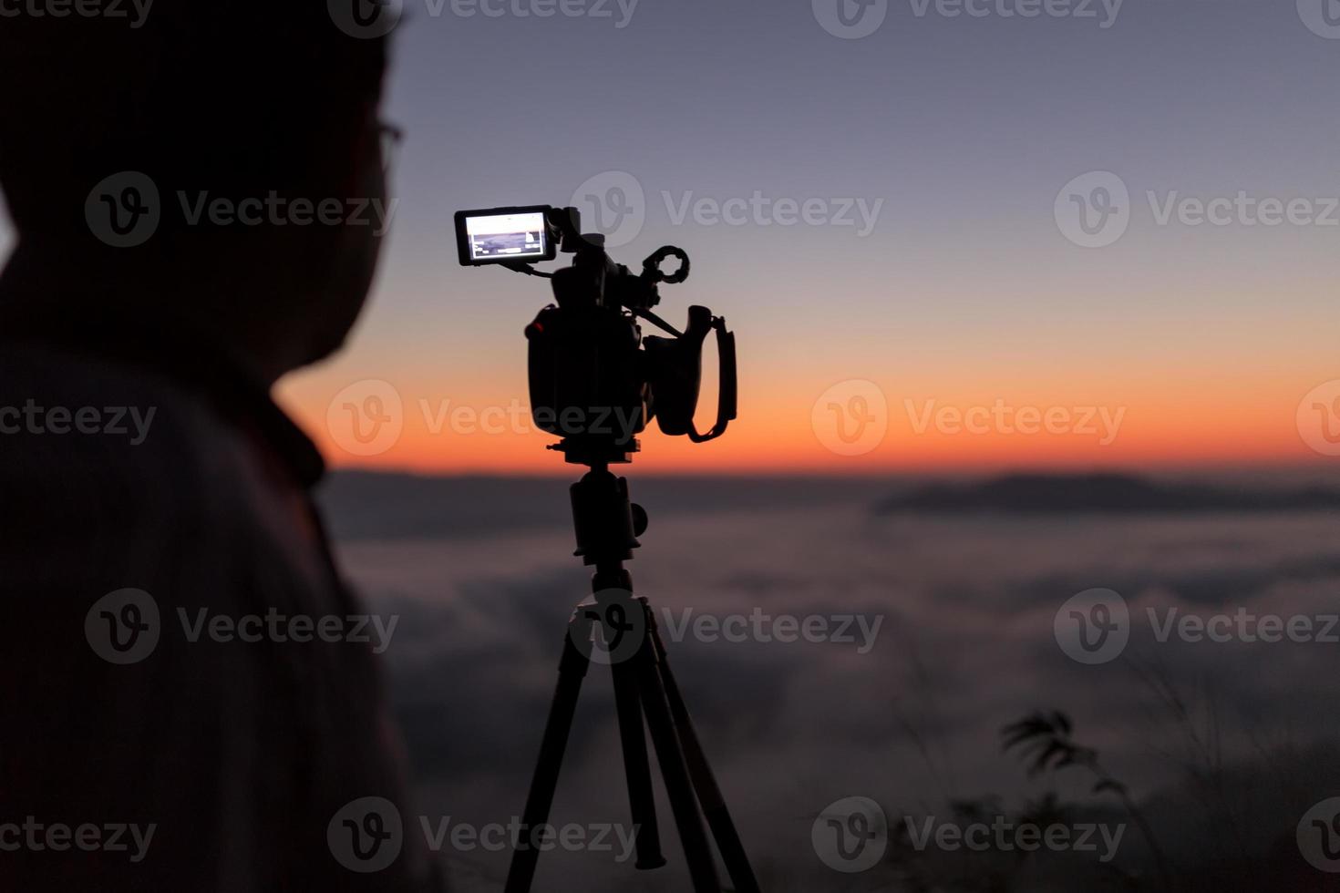 cameraman en videocamera-operator die met zijn apparatuur aan het werk is om een mistig landschap bij zonsopgang te fotograferen foto