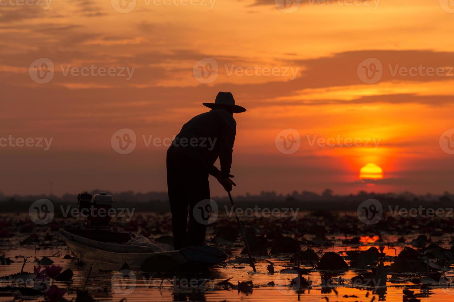 de silhouetvisser die hoed draagt en aan een boot werkt tijdens zonsopgang bij het meer udon thani, thailand. foto
