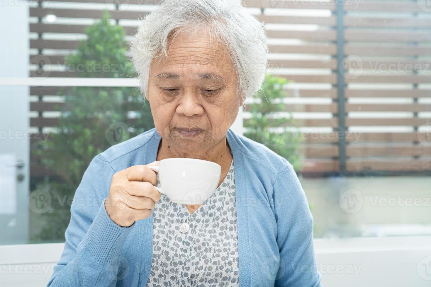 Aziatische senior of oudere oude vrouw die mok vasthoudt en 's ochtends thuis koffie drinkt, gezond sterk medisch concept foto