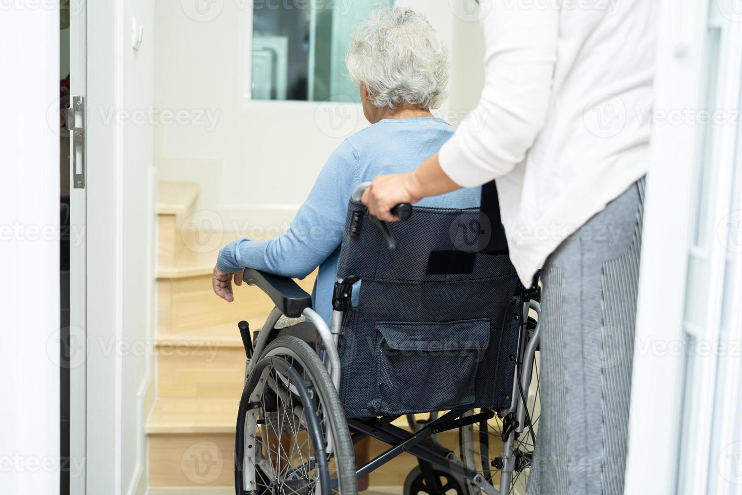 verzorger helpt aziatische of oudere oude vrouw die in een rolstoel zit, de trap op gaat in huis. foto