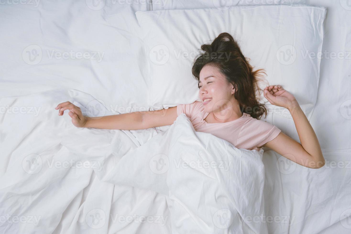 jonge vrouw slaapt goed in bed en knuffelt zacht wit kussen. tienermeisje rusten. goede nachtrust concept. meisje dat een pyjama draagt, slaapt 's ochtends op een bed in een witte kamer. warme toon. foto