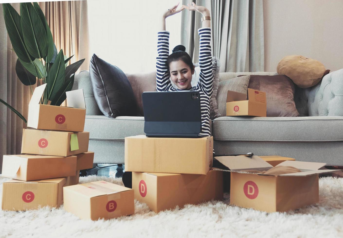 gelukkige succesvolle zakenvrouw met armen omhoog werken met laptop en kartonnen doos op tafel in kantoor aan huis. zakelijk online en leveringsconcept. foto