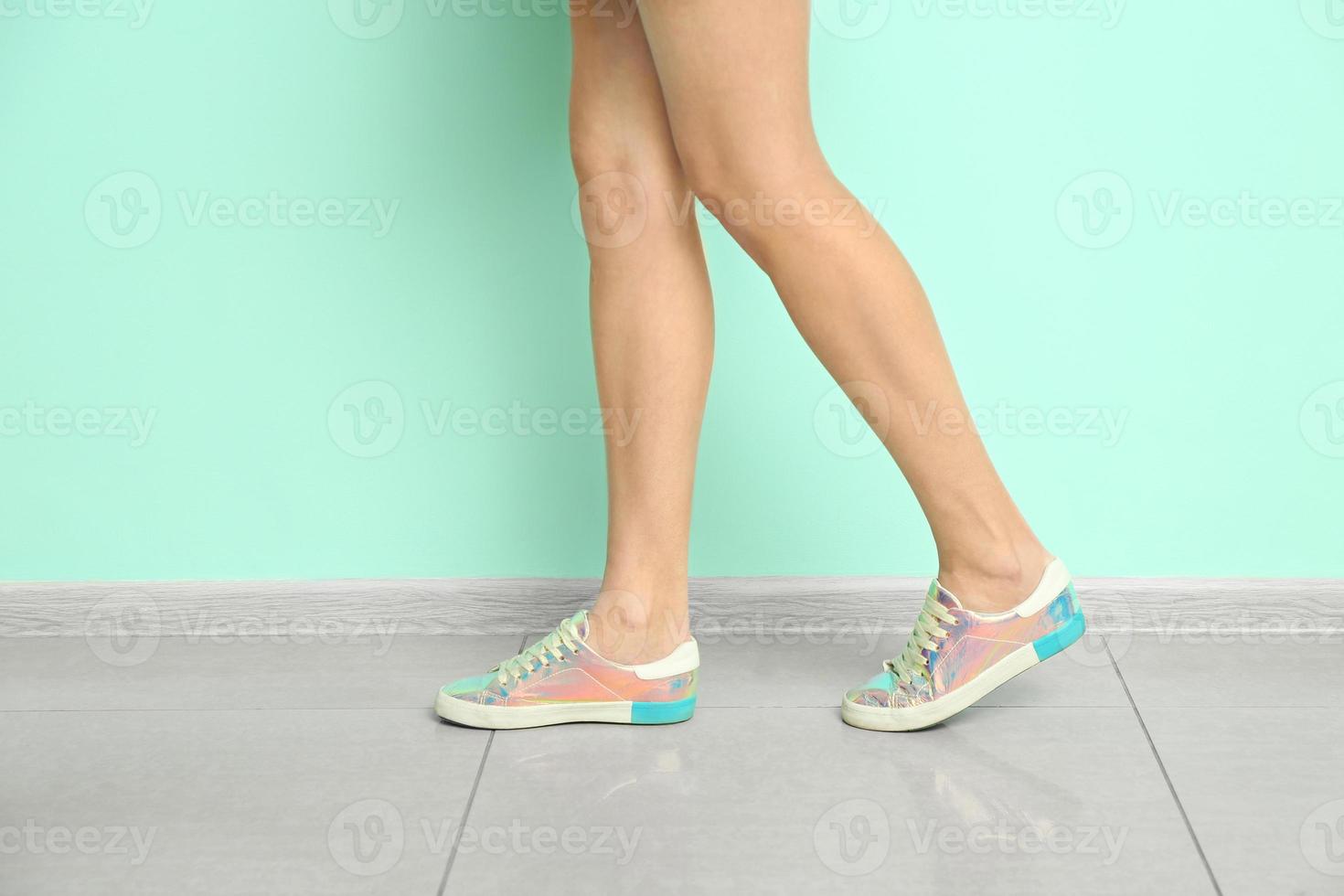 jonge vrouw in stijlvolle vrijetijdsschoenen in de buurt van kleurmuur foto