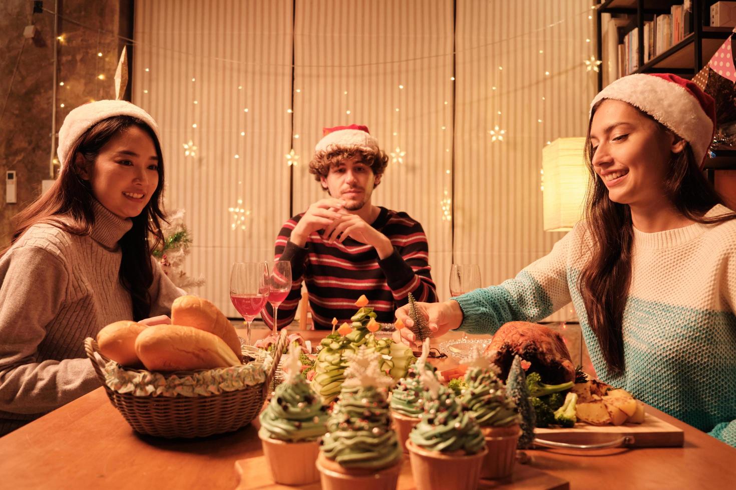 vrienden genieten van een gezellig diner aan een tafel met speciale maaltijden, een jonge vrouw pakt het voedselornament op in de eetkamer van het huis, versierd voor het kerstfestival en het nieuwjaarsfeest. foto