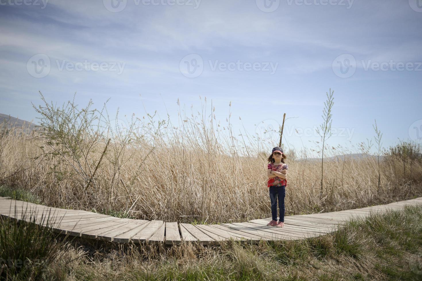 klein meisje loopt op een pad van houten planken in een wetland foto