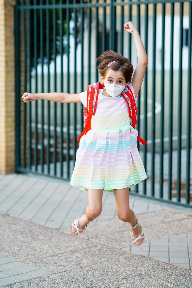 meisje dat een masker draagt, springt van vreugde terug naar school. foto