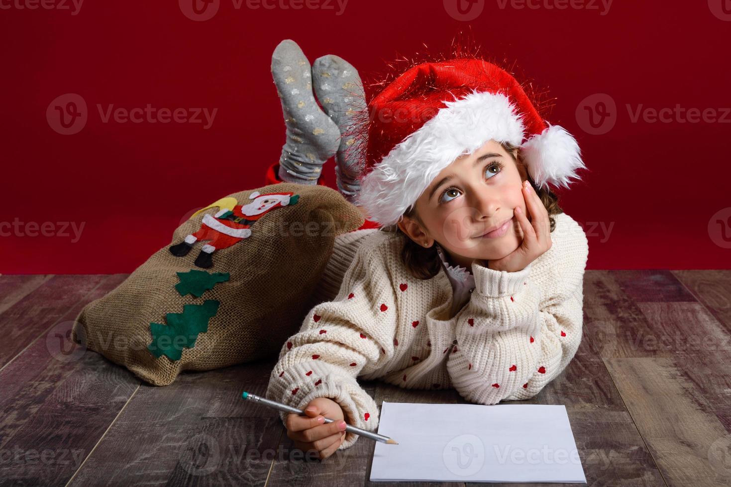 schattig klein meisje met een kerstmuts die een kerstbrief schrijft foto