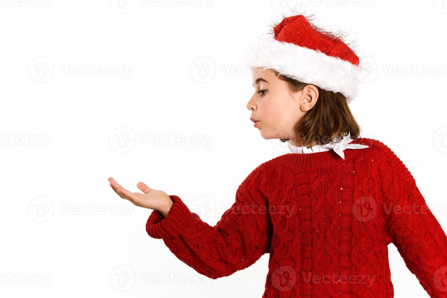 schattig klein meisje met een kerstmuts die naar haar hand blaast foto