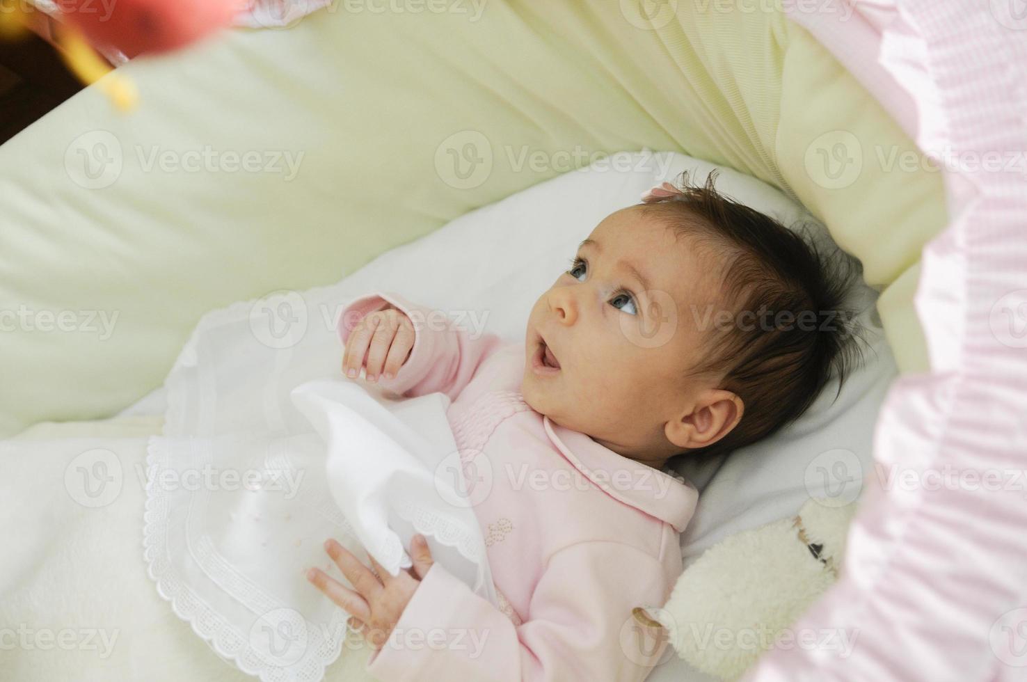 babymeisje kijkt naar een pop in zijn wieg foto