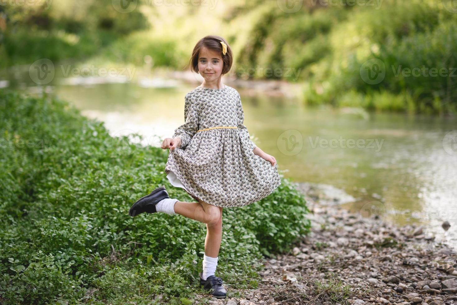 klein meisje in de natuurstroom die een mooie jurk draagt foto