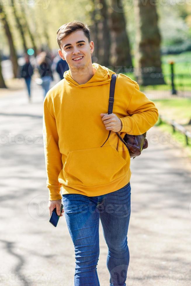 jonge stedelijke man met smartphone wandelen in de straat in een stadspark in londen. foto