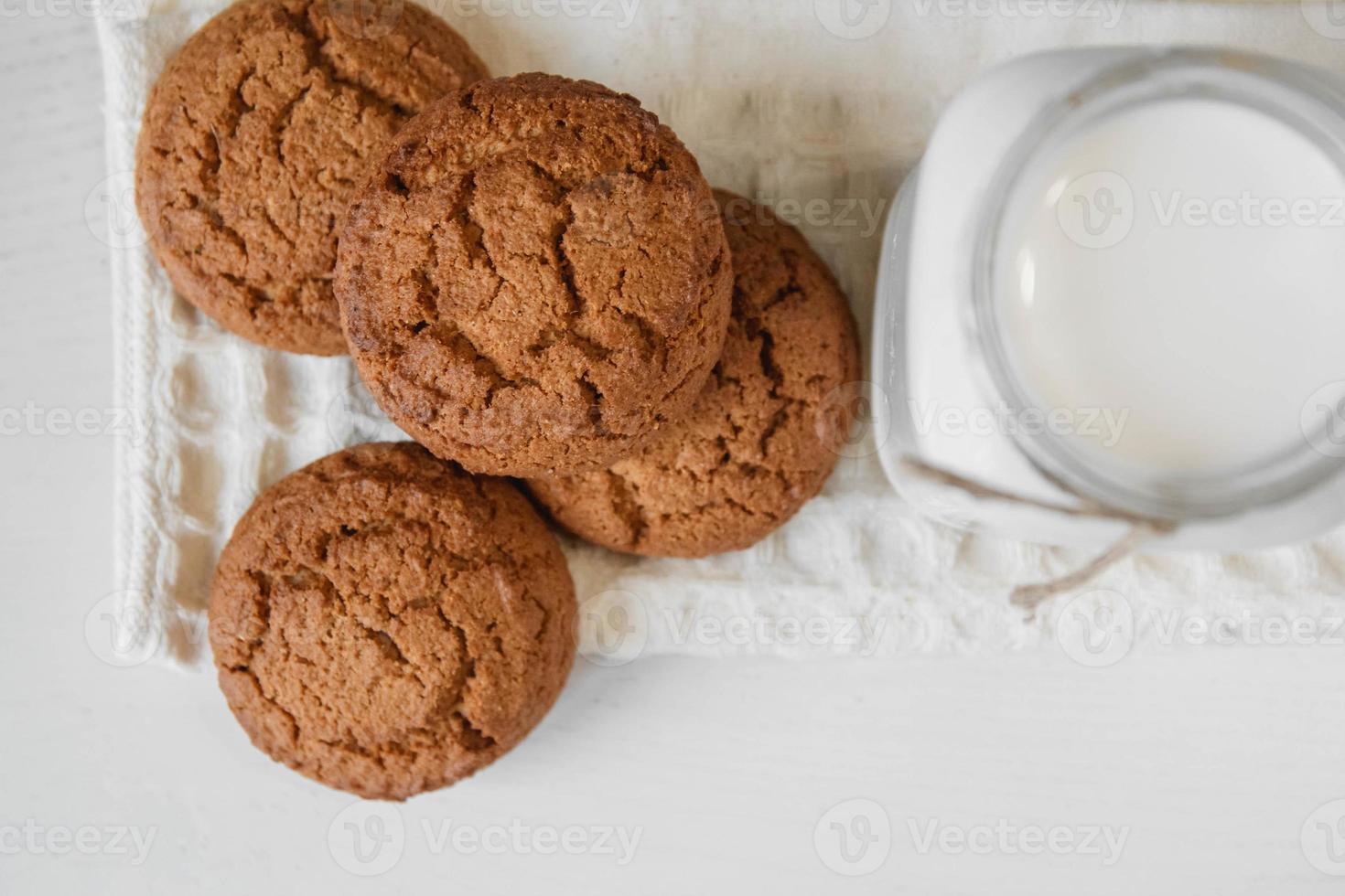 melk in glazen pot en havermoutkoekjes in de buurt van servet op witte tafel foto