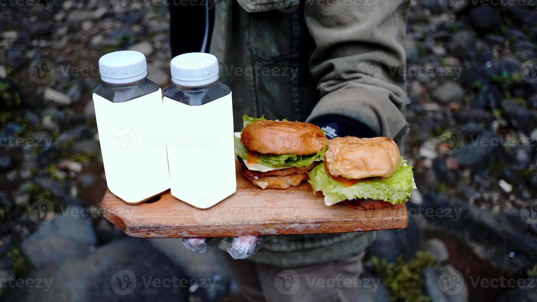 een mannelijke chef-kok die twee hamburgers en twee flessen drankjes bij zich heeft aan de rand van de waterval foto