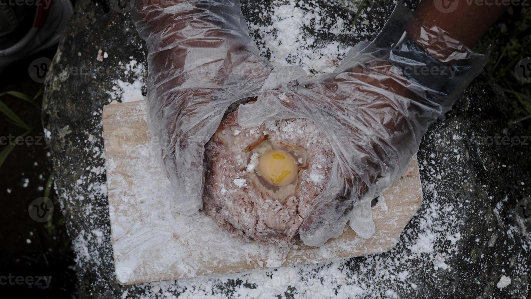 een jonge chef-kok maakt hamburger-vuldeeg aan de rand van een waterval foto