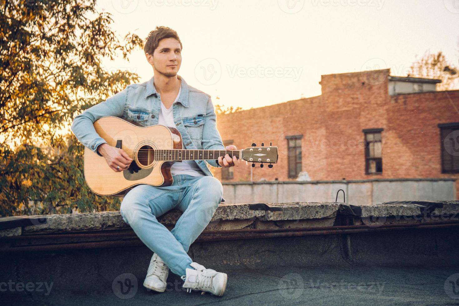 jonge man die gitaar speelt in de stad op de achtergrond van zonnestralen foto