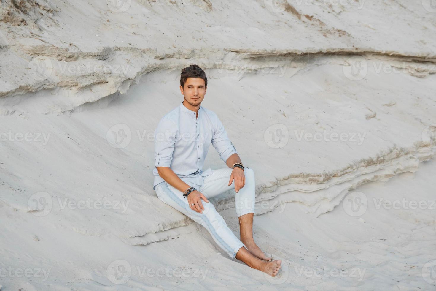 man in lichte kleding zit in woestijn foto