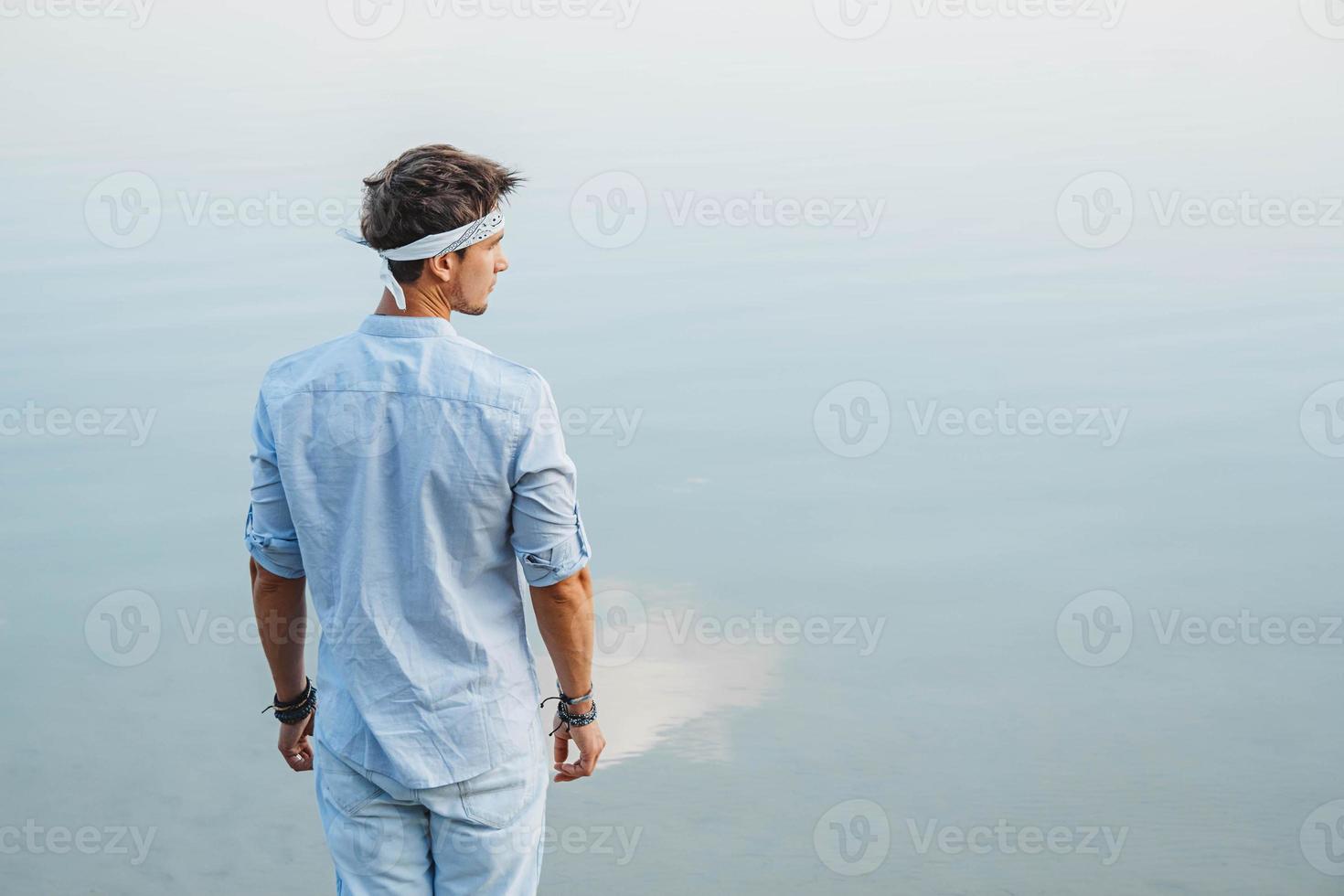 man gekleed in lichte kleding kijkt naar de waterreflex van blauwe lucht foto