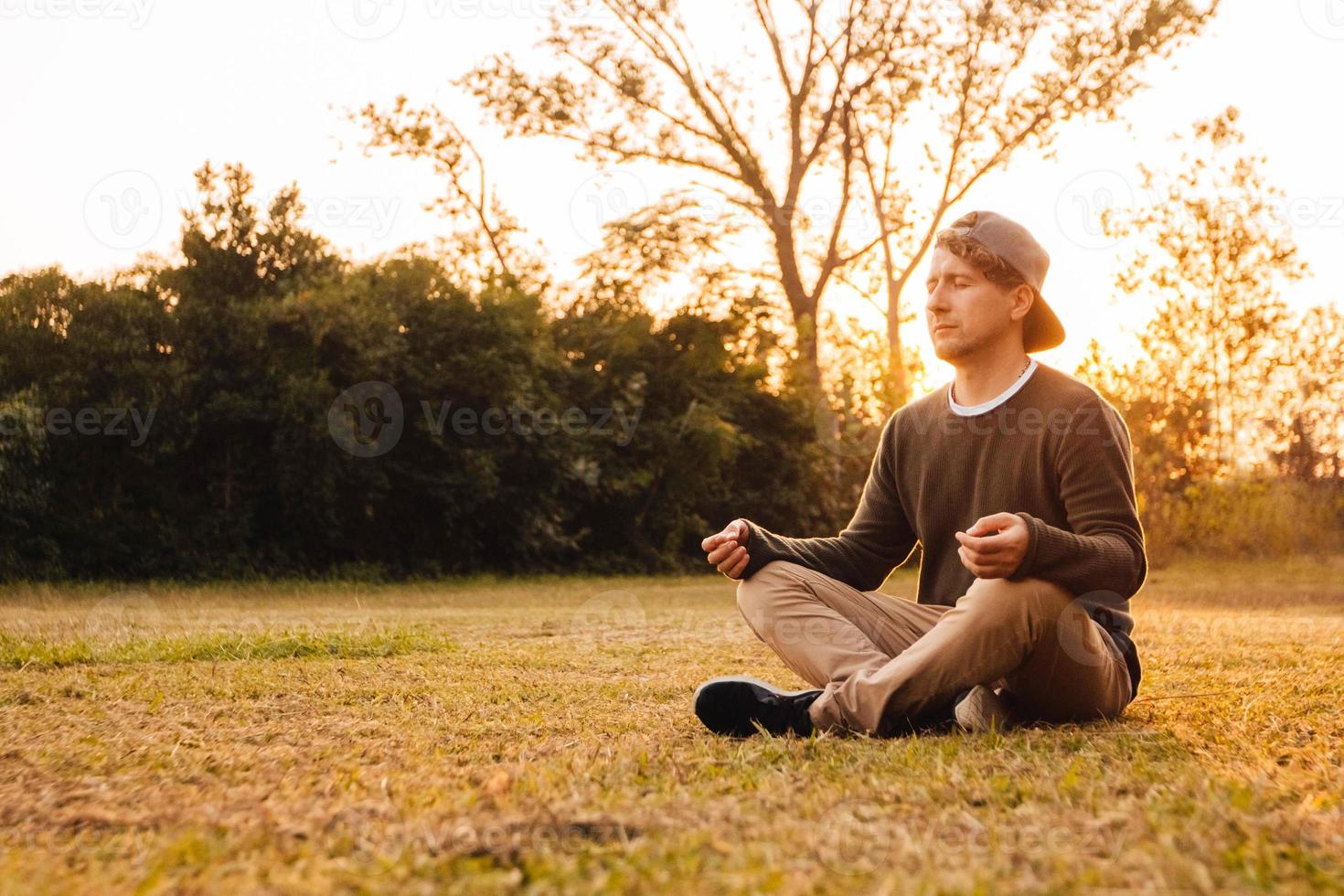 man in een meditatieve positie zit op een grasveld op een achtergrond van bos en zonsondergang foto