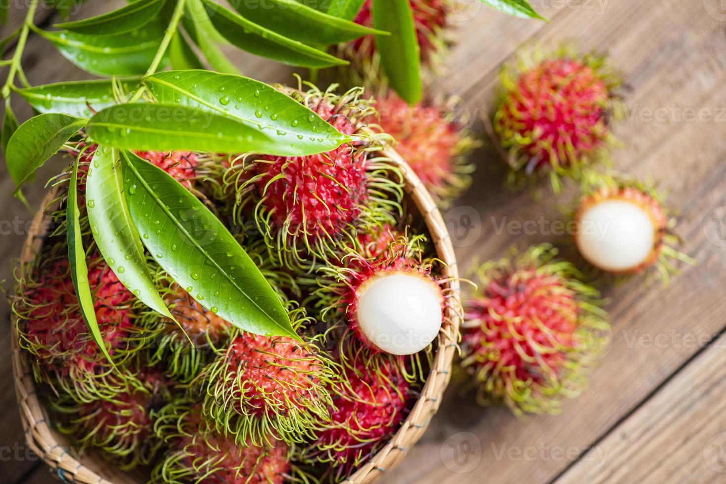 verse en rijpe ramboetan zoet tropisch fruit gepelde ramboetan met bladeren, ramboetan fruit op mand en houten achtergrond oogst uit de tuin foto