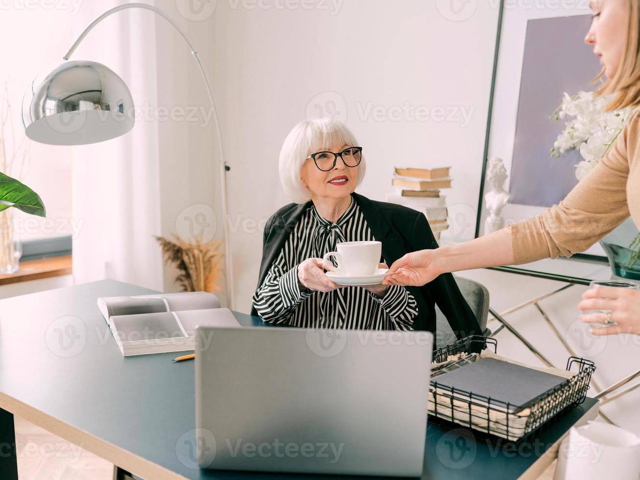 jonge assistent bracht een kopje koffie naar de baas op kantoor. bedrijf, communicatie, werk, leeftijden, samenwerking, mentorconcept foto