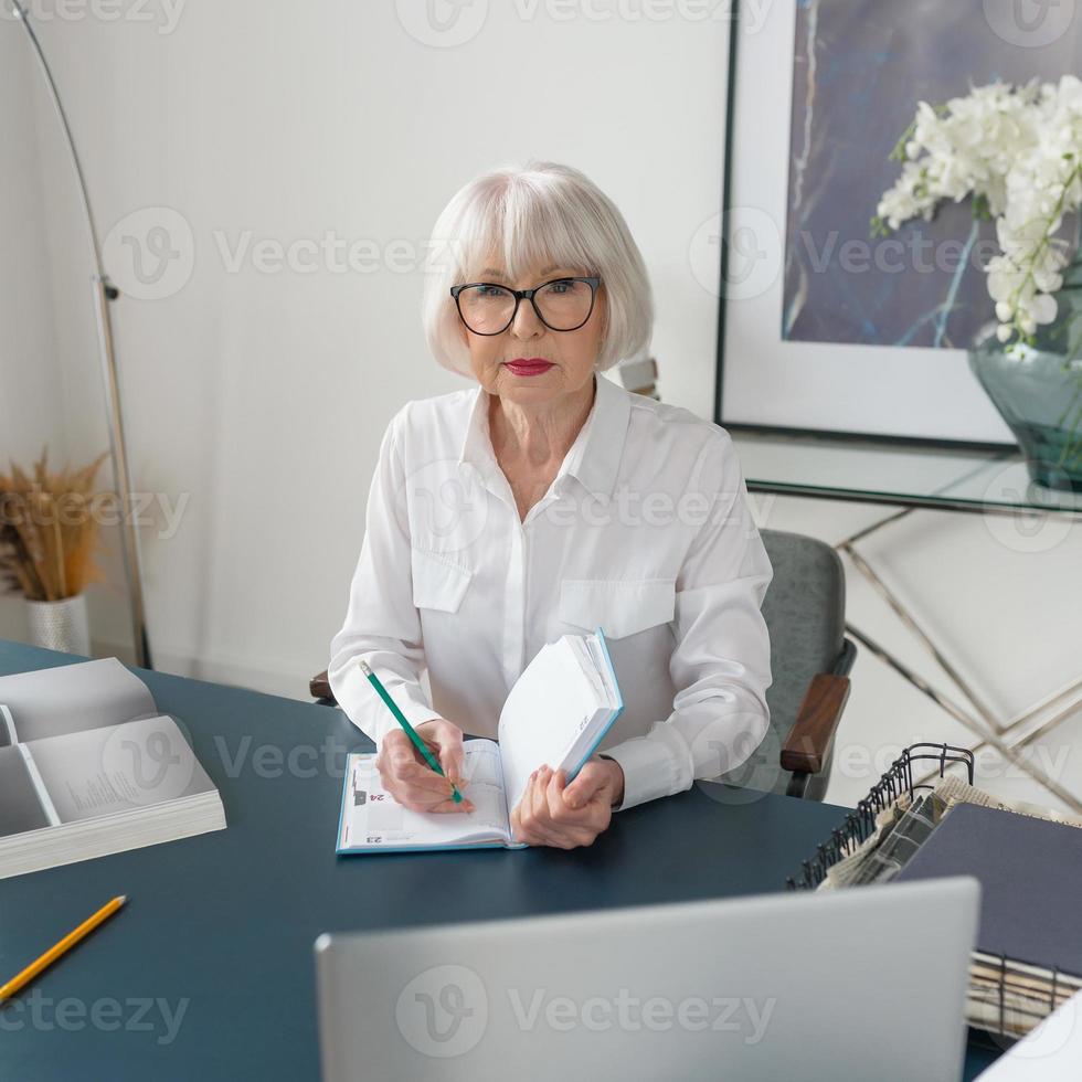 moe senior mooie grijze haren vrouw in witte blouse lezen van documenten op kantoor. werk, senioren, problemen, een oplossing vinden, ervaringsconcept foto