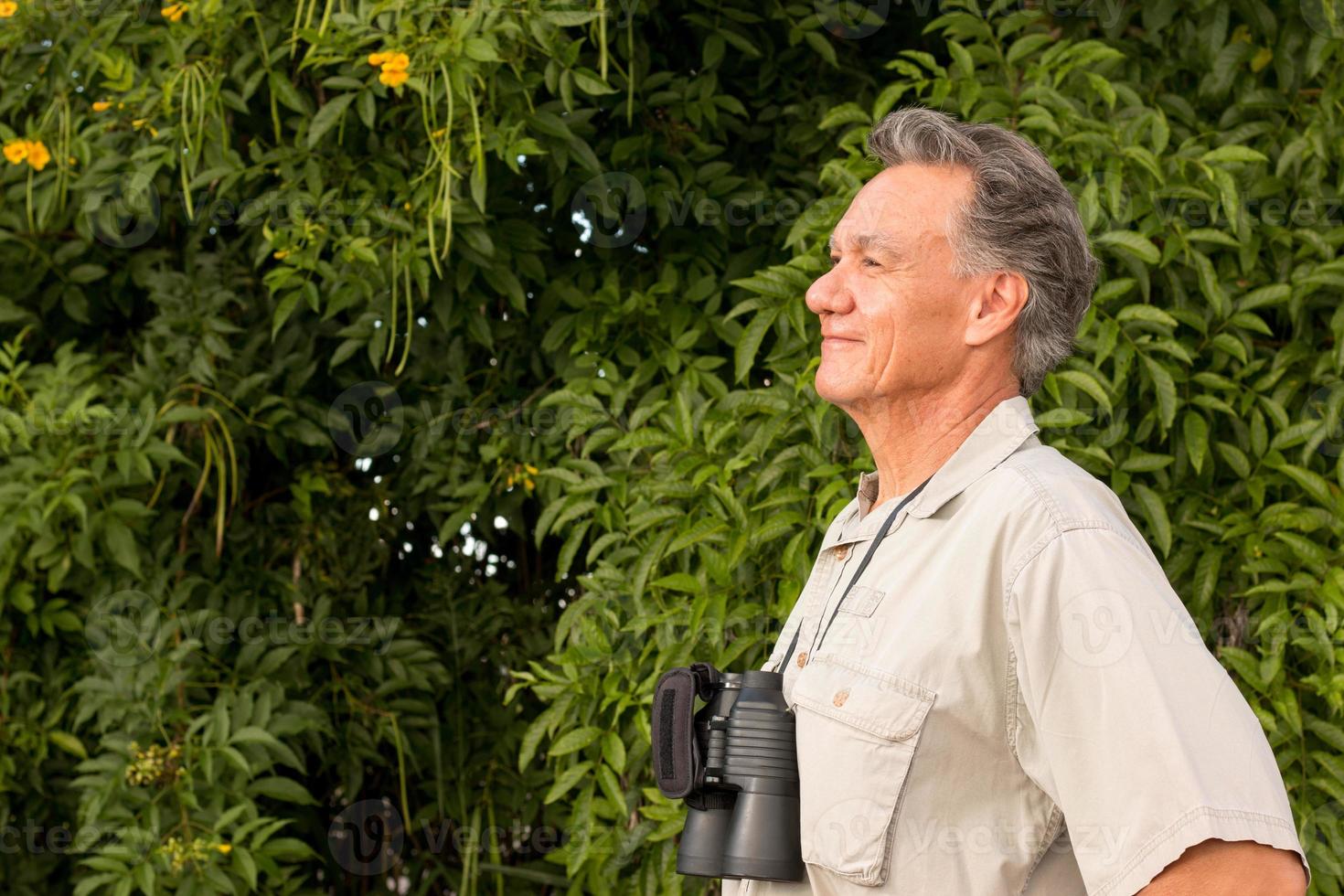 senior man buiten genietend van de natuur kijkend door een verrekijker foto