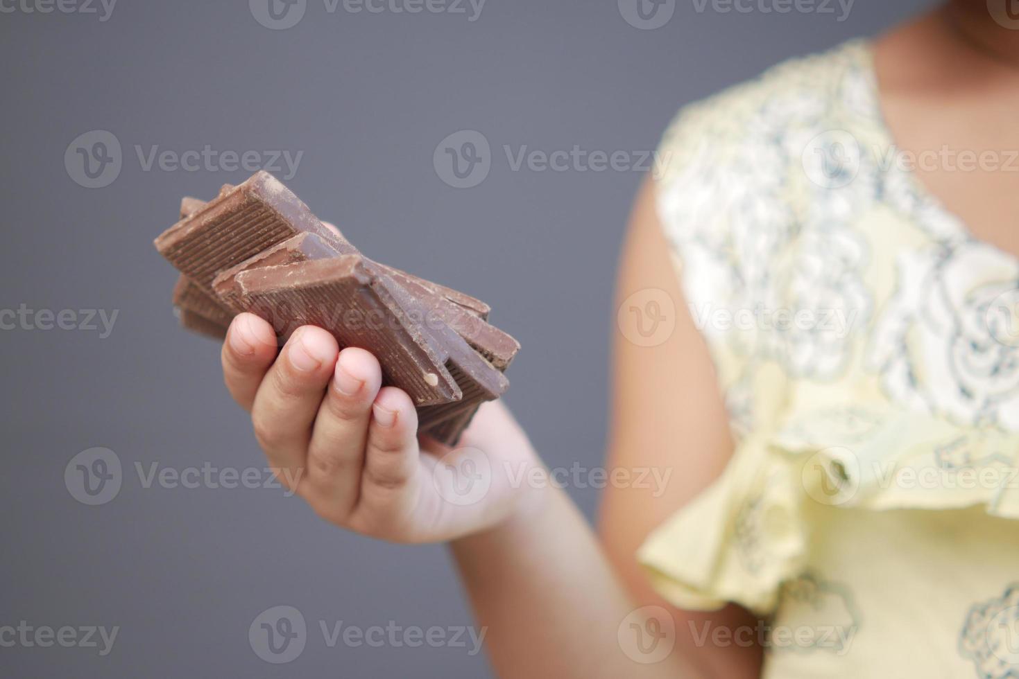 kind meisje hand plukken donkere chocolade tegen grijze achtergrond foto