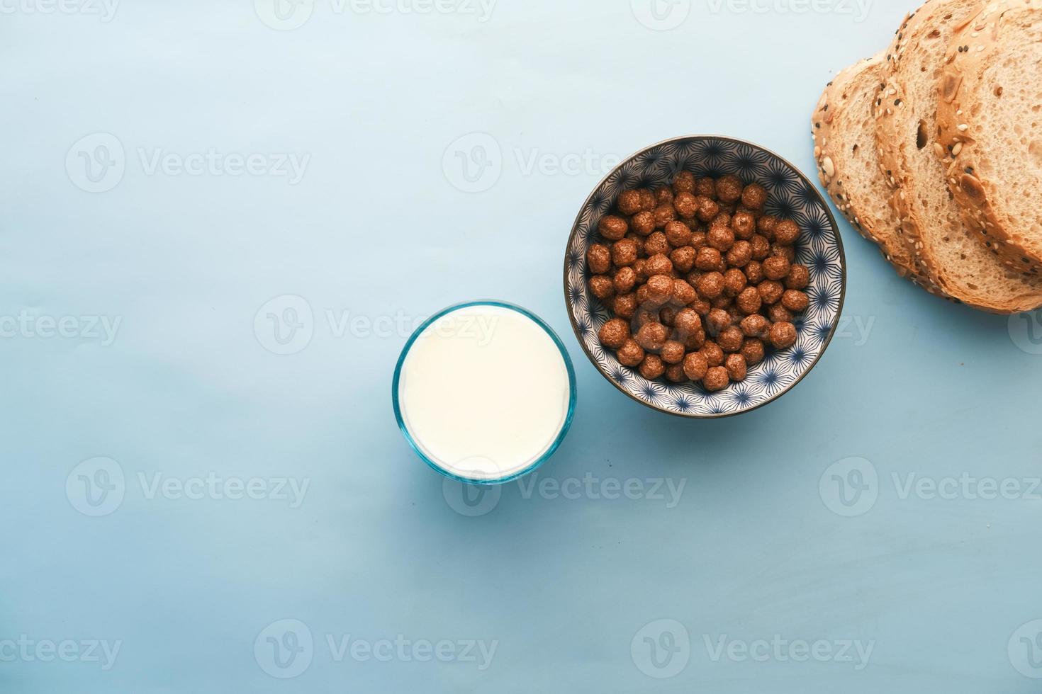 bovenaanzicht van chocolade cornflakes, melk en brood op blauw foto